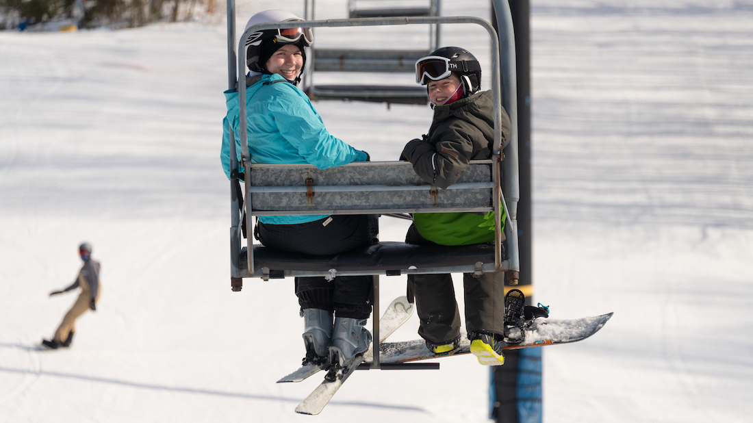 skier and snowboarder looking back riding chair lift